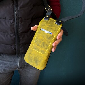 May include: A yellow leather phone case with a black strap. The case has a card slot and is worn over the shoulder.