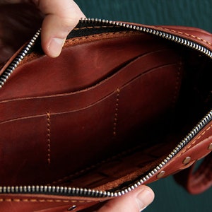 May include: A brown leather zippered pouch with multiple interior pockets. The pouch is open and the interior is visible.