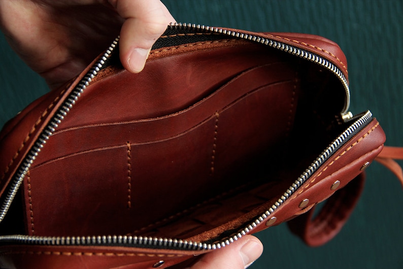May include: A brown leather zippered pouch with multiple interior pockets. The pouch is open and the interior is visible.
