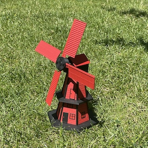 May include: A red and black windmill with a small house-like base. The windmill has four blades and is made of wood. The house has a black roof and white windows.