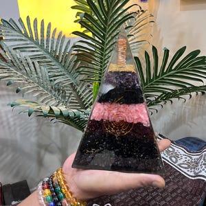 Puede incluir: Una pir&aacute;mide transparente hecha de cristales en capas, incluyendo amatista, cuarzo rosa, turmalina negra y cuarzo transparente. Una bobina de alambre de cobre est&aacute; incrustada en el centro de la pir&aacute;mide.