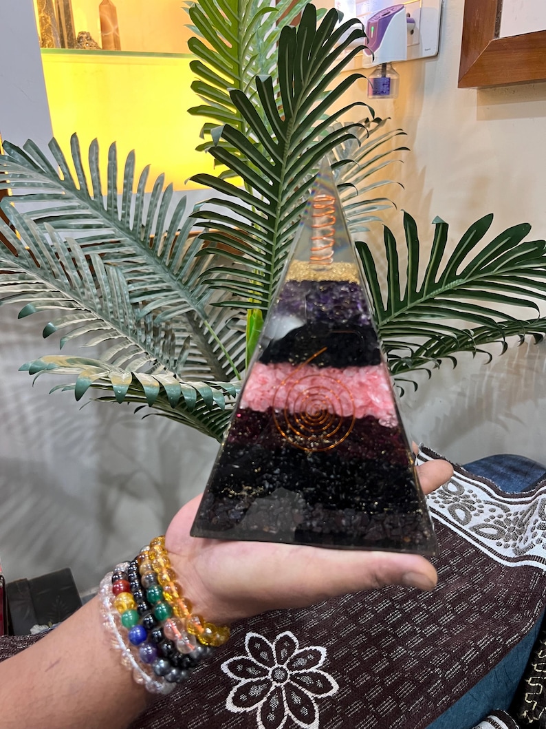 Puede incluir: Una pir&aacute;mide transparente hecha de cristales en capas, incluyendo amatista, cuarzo rosa, turmalina negra y cuarzo transparente. Una bobina de alambre de cobre est&aacute; incrustada en el centro de la pir&aacute;mide.