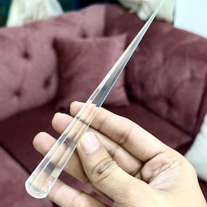 Puede incluir: Una varita de vidrio transparente con una punta puntiaguda. La varita se sostiene en una mano.