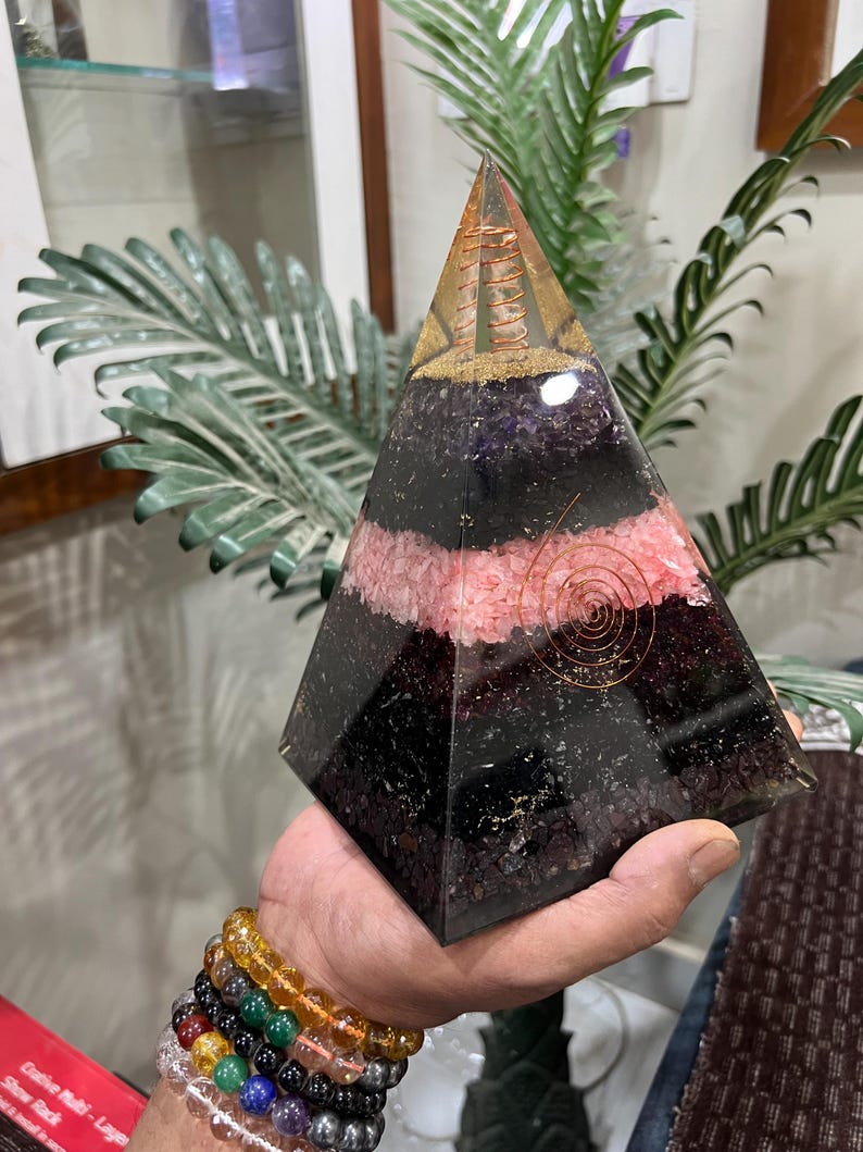 Puede incluir: Una pir&aacute;mide transparente hecha de cristales en capas. La pir&aacute;mide est&aacute; hecha de amatista, cuarzo rosa y turmalina negra. Una bobina de alambre de cobre est&aacute; incrustada en la pir&aacute;mide.
