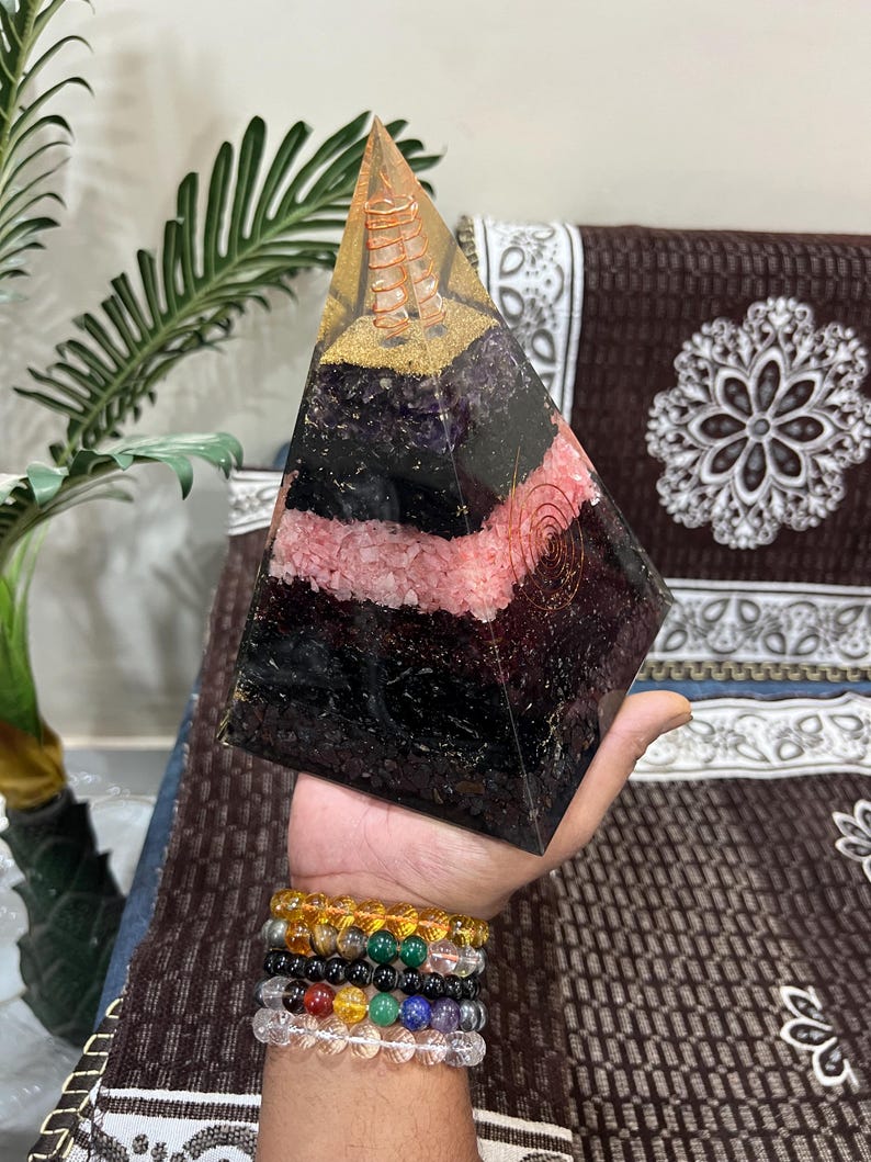 Puede incluir: Una gran pir&aacute;mide de cristal multicolor con una bobina de alambre de cobre en su interior. La pir&aacute;mide est&aacute; hecha de amatista, cuarzo rosa y obsidiana negra.