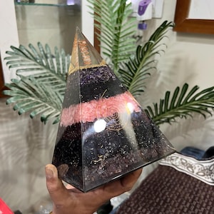 Puede incluir: Una pir&aacute;mide de cristal en capas con una espiral de alambre de cobre en su interior. La pir&aacute;mide est&aacute; hecha de cristales de amatista, cuarzo rosa, turmalina negra y cuarzo transparente. La pir&aacute;mide mide aproximadamente 15 cm de alto.