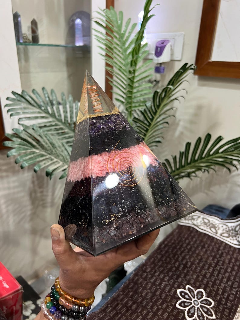 Puede incluir: Una pir&aacute;mide de cristal en capas con una espiral de alambre de cobre en su interior. La pir&aacute;mide est&aacute; hecha de cristales de amatista, cuarzo rosa, turmalina negra y cuarzo transparente. La pir&aacute;mide mide aproximadamente 15 cm de alto.