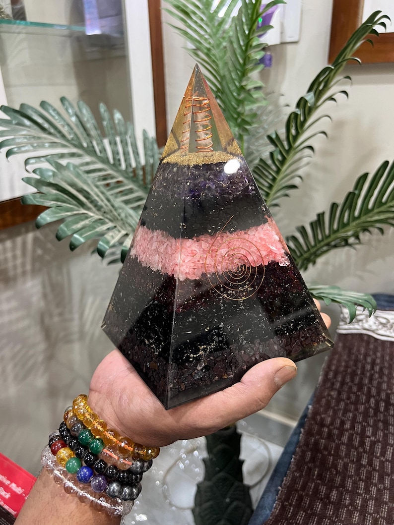 Puede incluir: Una pir&aacute;mide de cristal en capas con una espiral de alambre de cobre en su interior. La pir&aacute;mide est&aacute; hecha de cristales de amatista, cuarzo rosa y obsidiana negra. La pir&aacute;mide mide aproximadamente 15 cm de alto.
