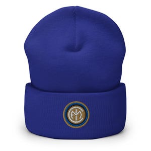 Puede incluir: Un gorro de punto azul con un logotipo bordado en oro y azul. El logotipo es un círculo con un "FC" blanco en su interior.