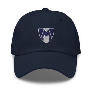 May include: A navy blue baseball cap with an embroidered white and blue shield logo featuring the letter "M".