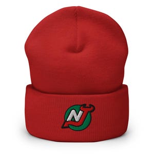 Puede incluir: Gorro de punto rojo con un logotipo bordado en verde, blanco y rojo de un "NJ" estilizado con una llave.