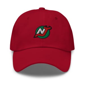 Puede incluir: Gorra de béisbol roja con un logotipo bordado en verde, blanco y rojo de una "N" estilizada con llamas en la parte superior.