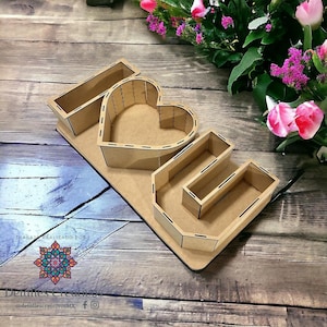 Puede incluir: Corte de madera de la palabra "LOVE" con un corazón en el centro. Cada letra tiene un pequeño compartimento para guardar objetos pequeños. El corte está hecho de madera marrón y tiene un acabado desgastado.