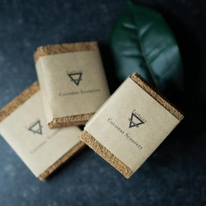 May include: Three brown coconut scrubbers with a triangular logo and the text "Earthies Coconut Scourers" on the front.