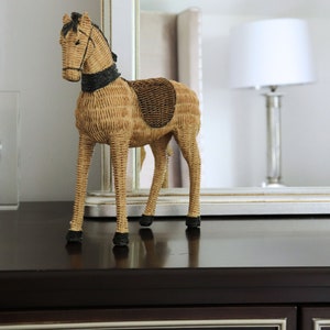 Puede incluir: Figura de caballo de mimbre tejido con crin, brida y silla de montar negras. El caballo decorativo es de color beige y marr&oacute;n, de pie sobre una superficie marr&oacute;n oscuro. La figura es un adorno decorativo para el hogar.