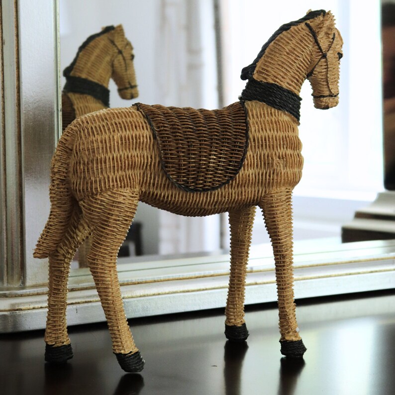 Puede incluir: Figura decorativa de caballo de mimbre. El caballo est&aacute; tejido en color marr&oacute;n claro con una silla de montar marr&oacute;n oscuro y detalles negros en la crin, la cola y los cascos. El caballo est&aacute; sobre una superficie oscura.