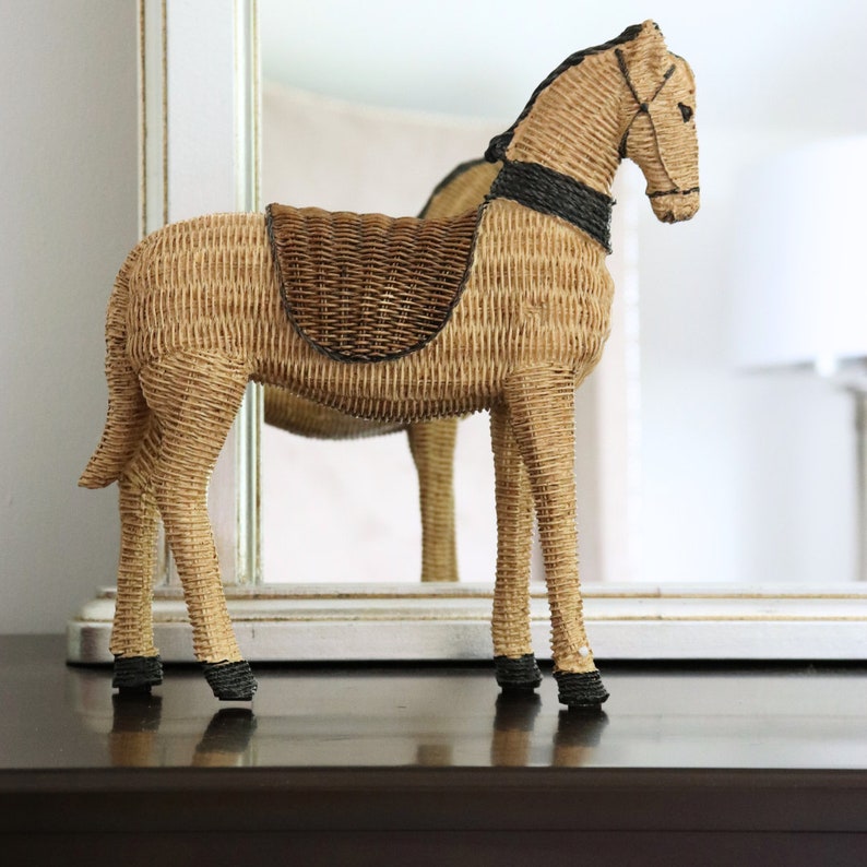 Puede incluir: Figura decorativa de caballo de mimbre. El caballo es de color beige con una silla de montar marr&oacute;n oscuro y detalles negros en la crin, la brida y los cascos. El caballo est&aacute; de pie sobre cuatro patas y se refleja en un espejo detr&aacute;s.