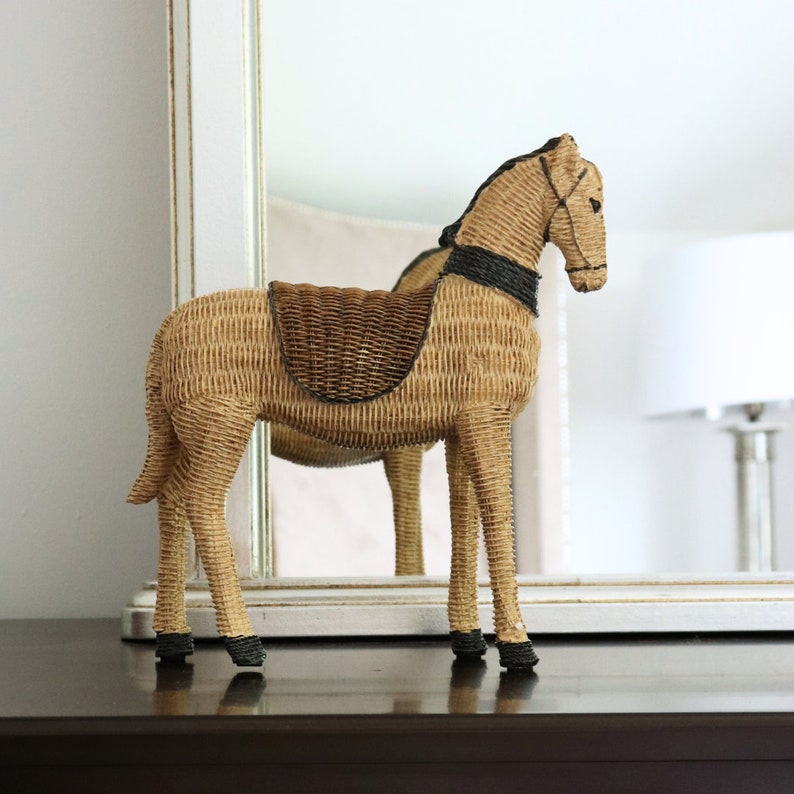 Puede incluir: Figura decorativa de caballo de mimbre. El caballo es de color marr&oacute;n claro con una silla de montar marr&oacute;n m&aacute;s oscura y detalles negros en la crin, la brida y los cascos. La figura est&aacute; sobre una superficie marr&oacute;n oscuro.
