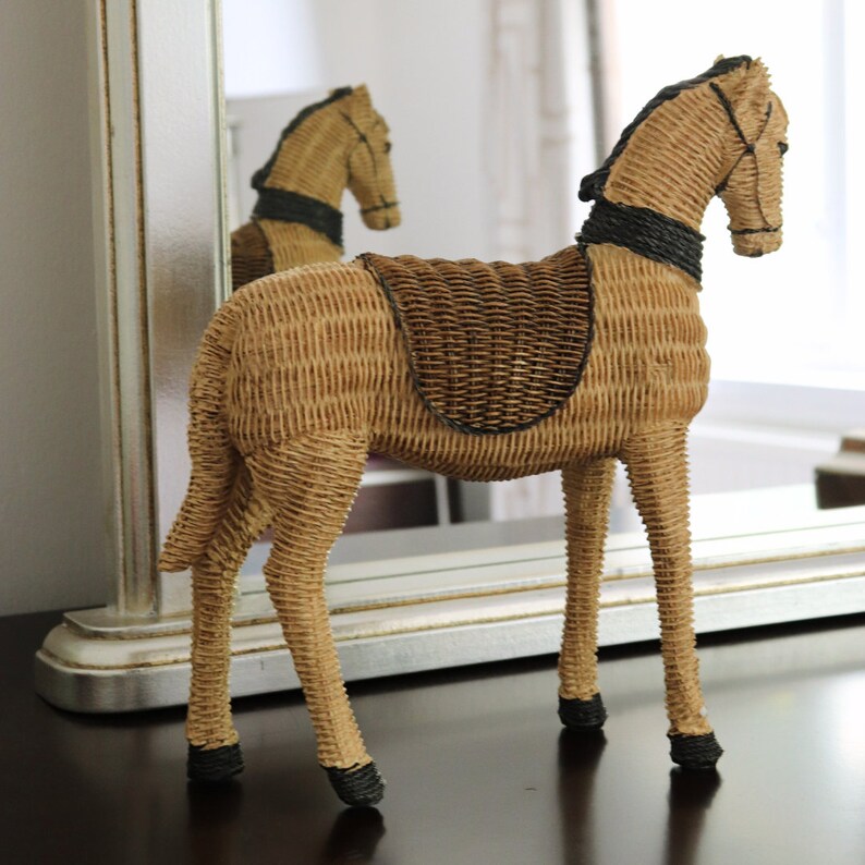 Puede incluir: Figura decorativa de caballo de mimbre. El caballo est&aacute; tejido con mimbre marr&oacute;n claro con una silla de montar y detalles en marr&oacute;n oscuro. El caballo est&aacute; de pie sobre cuatro patas y tiene una melena y cola detalladas.