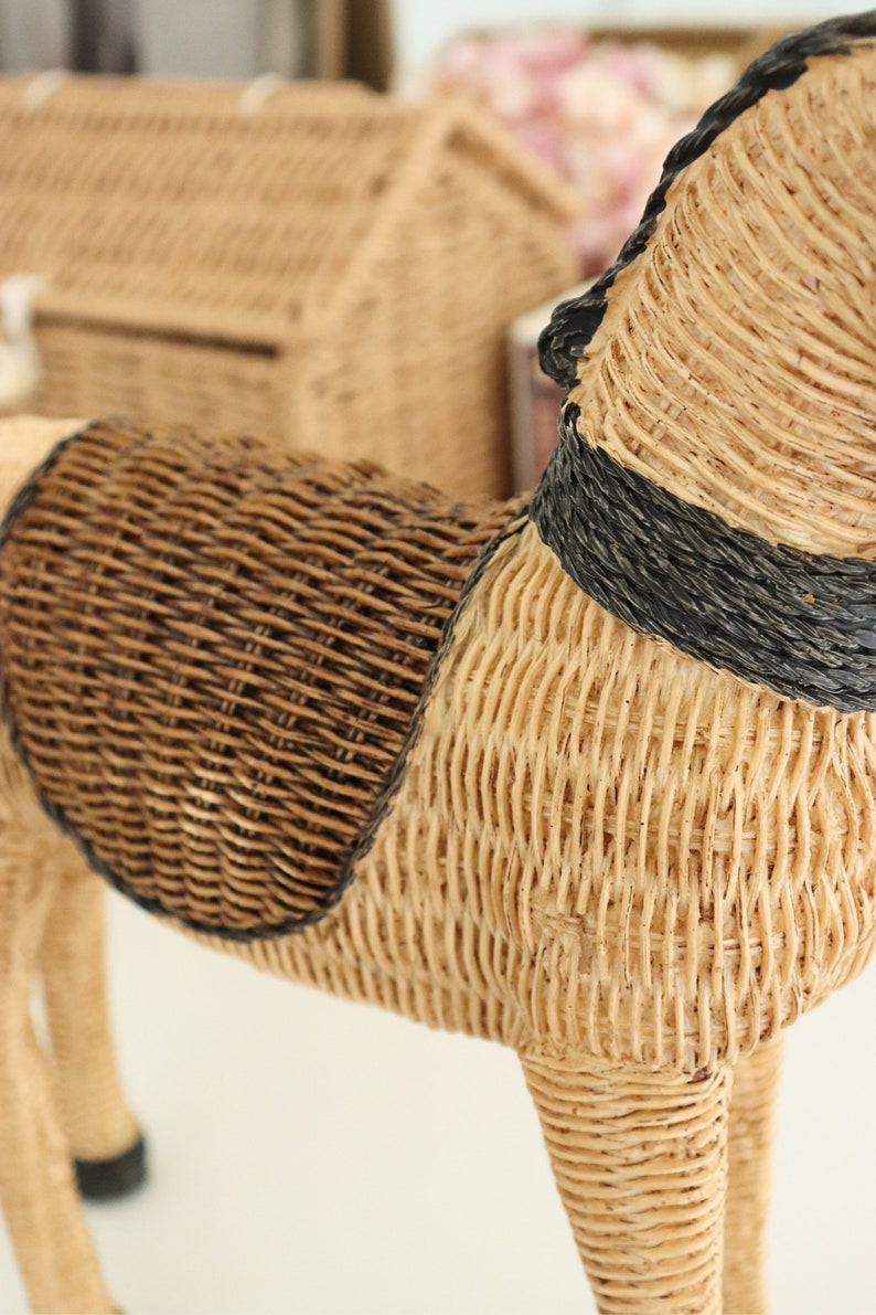 Puede incluir: Figura de caballo de mimbre tejido con una silla de montar marr&oacute;n oscuro y detalles negros. El caballo tiene un cuerpo de color canela claro y est&aacute; sobre cuatro patas. La figura est&aacute; hecha de materiales naturales y tiene un aspecto r&uacute;stico.