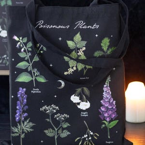 May include: Black tote bag featuring illustrations of various poisonous plants, including Deadly Nightshade and Foxglove. The bag has the words "Poisonous Plants" in white script. The design includes a crescent moon and stars.