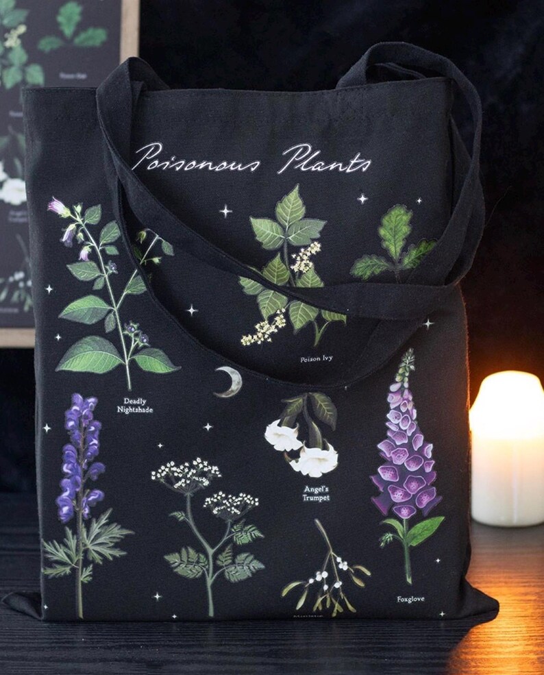 May include: Black tote bag featuring illustrations of various poisonous plants, including Deadly Nightshade and Foxglove. The bag has the words "Poisonous Plants" in white script. The design includes a crescent moon and stars.