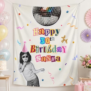 May include: A white fabric birthday backdrop featuring a large disco ball at the top, colorful confetti, and a gold balloon dog. The text reads Happy 30th Birthday Sasha in a multi-colored collage font, with a photo of a person wearing a party hat.