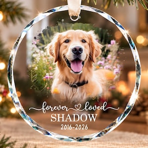 May include: A circular glass ornament with a faceted edge featuring a photograph of a golden retriever dog. The text "forever loved", the name "SHADOW", and the years "2016-2026" are printed in white on the lower portion of the ornament.