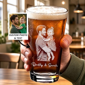 May include: A pint glass filled with beer, featuring a custom etched image of a father and child. The glass also has the text "Daddy & Sarah" etched on it. A small photo with the text "CUSTOM PHOTO & TEXT" is next to the glass.