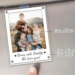 May include: Clear acrylic car visor photo holder with a family photo. The photo is of a family of five. The text "Drive safe Daddy We love you!" is printed below the photo in a script font.