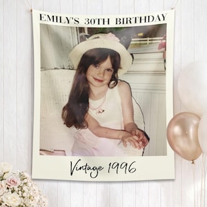 May include: A banner with a vintage photo of a young girl wearing a hat, with the text "Emily's 30th Birthday" at the top and "Vintage 1996" at the bottom. White and gold balloons are tied to the banner.