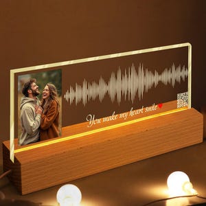 May include: A personalized LED light-up photo frame with a wooden base. The frame features a couple's photo, a sound wave design, and the text "You make my heart smile." The base has a warm, glowing light.
