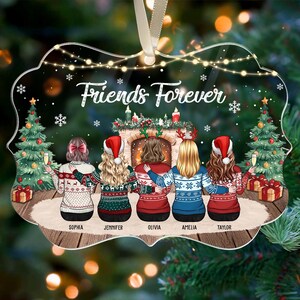 May include: Clear acrylic Christmas ornament with the words "Friends Forever" and illustrations of five friends in sweaters. The ornament features a fireplace, Christmas trees, and gift boxes. A cream-colored ribbon is attached for hanging.