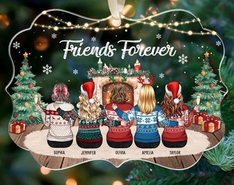 May include: Clear acrylic Christmas ornament with the words "Friends Forever" and illustrations of five friends in sweaters. The ornament features a fireplace, Christmas trees, and gift boxes. A cream-colored ribbon is attached for hanging.