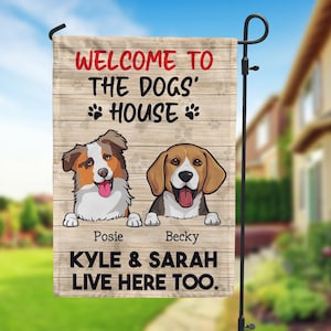 May include: A wooden sign with the text "Welcome to the Dogs' House" and paw prints. Two cartoon dogs, a brown and white Australian Shepherd named Posie and a brown and white Beagle named Becky, are peeking over the top of the sign. The text "Kyle & Sarah Live Here Too." is at the bottom of the sign.