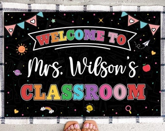 May include: A black chalkboard welcome sign with colorful lettering that reads "Welcome to Mrs. Wilson's Classroom". The sign is decorated with colorful stars, hearts, and other classroom-themed illustrations.