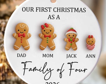 Peut inclure: Une décoration de Noël ronde en céramique blanche avec quatre figurines en pain d'épices nommées Dad, Mom, Jack et Ann. Le texte indique Our First Christmas As A Family of Four 2026. Elle comporte un ruban crème pour la suspendre par un anneau.