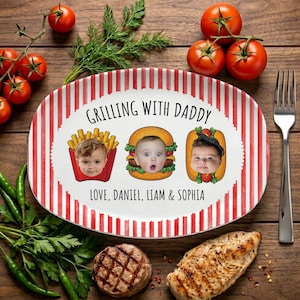 May include: Oval ceramic platter with red and white vertical stripes and the text "Grilling with Daddy." The platter features three cartoon images of babies as fries, a burger, and a hot dog. The names Daniel, Liam, and Sophia are also printed on the platter.