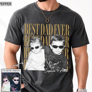 Pode incluir: T-shirt cinza escuro com foto personalizada e o texto dourado "BEST DAD EVER". A foto mostra duas crian&ccedil;as usando &oacute;culos de sol. A camisa tamb&eacute;m tem o texto "Sophia & Alex".