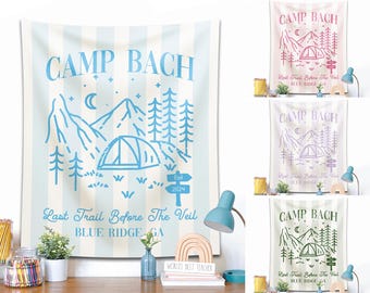 May include: A light blue and white striped wall tapestry with the text "CAMP BACH" and a mountain and tent graphic. The text "Last Trail Before The Veil BLUE RIDGE, GA" is also included. The tapestry is a decorative item.