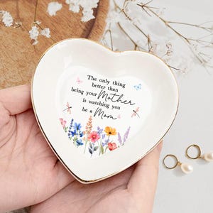 May include: White heart-shaped trinket dish with a gold rim. The dish features a floral design and the text "The only thing better than being your Mother is watching you be a Mom."