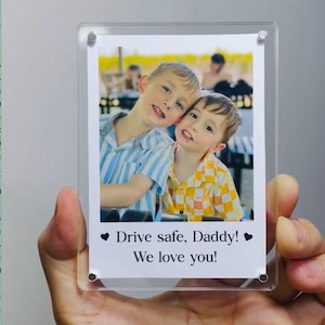 May include: A clear acrylic photo frame holding a printed photograph of two young boys smiling. The photo includes the text "Drive safe, Daddy! We love you!" in black font, with a heart symbol on each side.