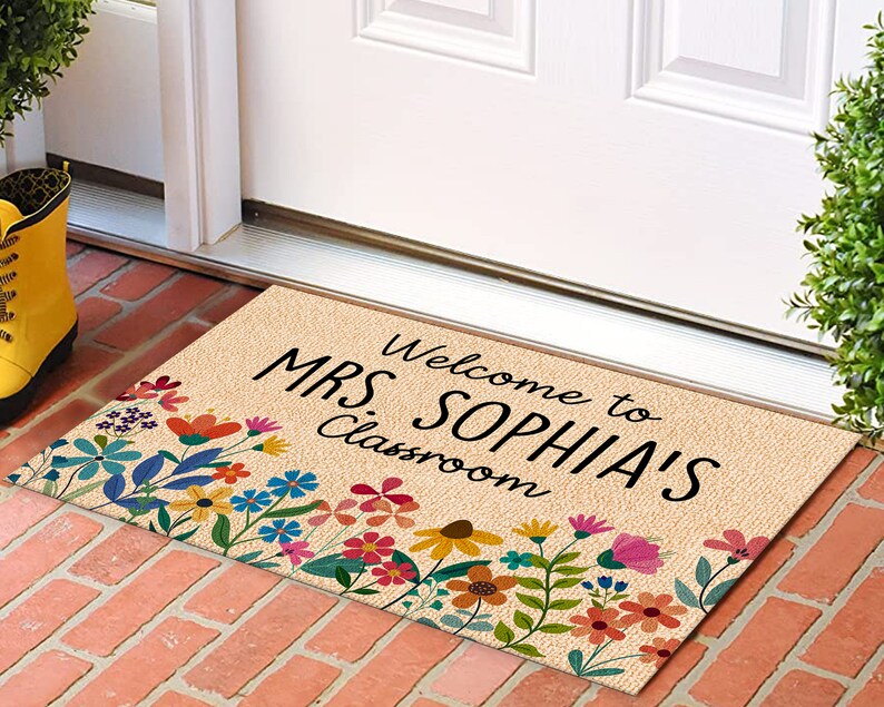 Może przedstawiać: Prostokątna wycieraczka z beżowym tłem i wielokolorową kwiatową obw&oacute;dką. Tekst "Welcome to MRS. SOPHIA'S Classroom" jest wydrukowany na czarno. Mata jest umieszczona na ceglanej powierzchni.