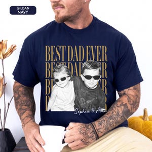 Pode incluir: Camiseta azul marinho com a frase dourada "BEST DAD EVER". Apresenta uma foto em preto e branco de duas crian&ccedil;as usando &oacute;culos de sol, com os nomes "Sophia & Alex" impressos abaixo.