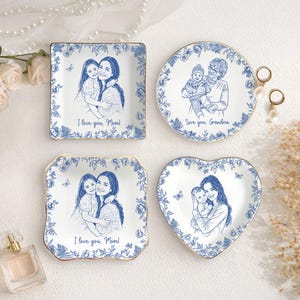 Puede incluir: Cuatro platos de cer&aacute;mica blanca con dise&ntilde;os florales azules y bordes dorados. Cada plato presenta un boceto azul de una persona o personas. El texto en los platos dice "I love you, Mom!" y "Love you, Grandma."