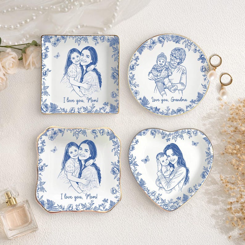 Puede incluir: Cuatro platos de cer&aacute;mica blanca con dise&ntilde;os florales azules y bordes dorados. Cada plato presenta un boceto azul de una persona o personas. El texto en los platos dice "I love you, Mom!" y "Love you, Grandma."