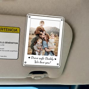 May include: A clear acrylic photo frame with a family photo, attached to a car visor. The photo shows a family of five, with the text "Drive safe Daddy, We love you!" in black script.