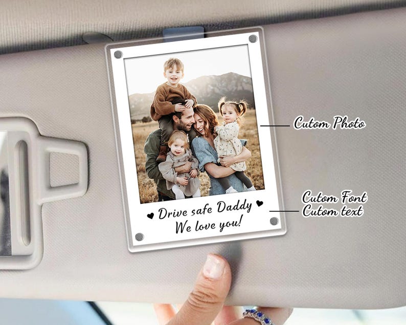 May include: Clear acrylic car visor photo holder with a family photo. The photo is of a family of five. The text "Drive safe Daddy We love you!" is printed below the photo in a script font.