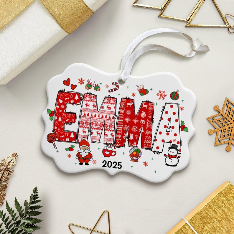 May include: A white ceramic Christmas ornament with the name "EMMA" in red. The letters are decorated with holiday patterns and images, including reindeer, snowflakes, and Santa Claus. The year "2025" is also displayed.