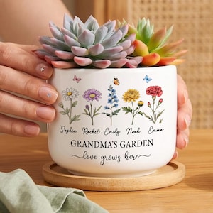 May include: White ceramic planter with a succulent arrangement. The planter is decorated with colorful flower illustrations and the text "GRANDMA'S GARDEN love grows here." The planter sits on a wooden coaster.